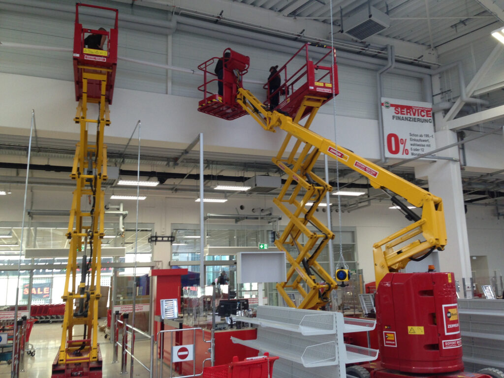 Gelbe Arbeitsbühne mit zwei Hebebühnen in einem Innenraum eines Geschäfts bei der Profi-Montage