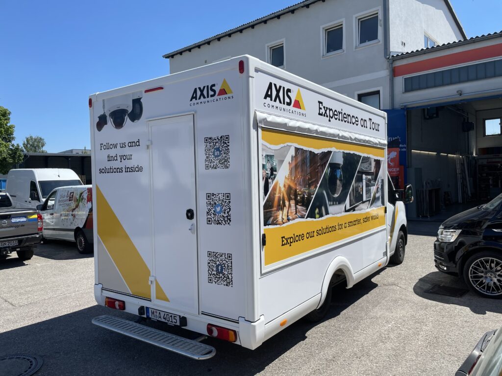 Weißes Fahrzeug von AXIS Communications mit Werbebeschriftung auf der Rückseite.