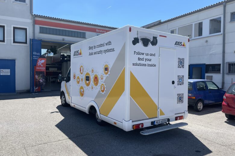 Weißer Transporter mit AXIS-Logo und Grafiken zu Sicherheitslösungen auf der Rückseite.