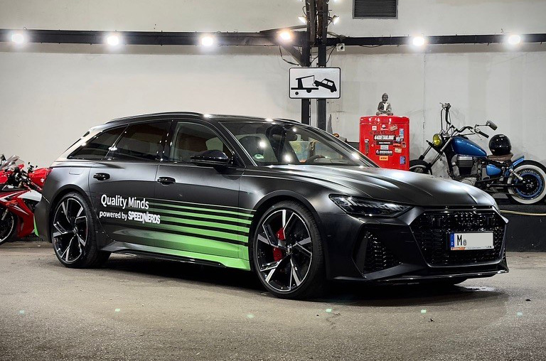 Schwarzer Audi A6 mit grüner Folierung und Aufschrift 'Quality Minds' in einer Garage.