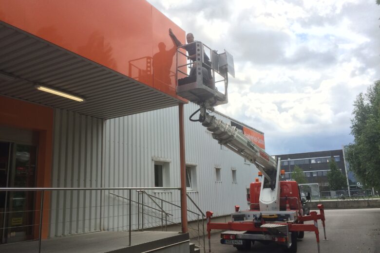 Arbeiter, die ein Firmenschild mit einem Hubsteiger an einer Wand anbringen.