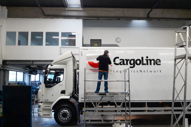 Ein Arbeiter bringt eine Beschriftung auf einem Lkw der CargoLine an.