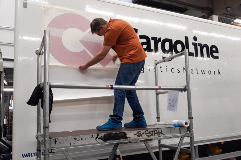 Ein Mitarbeiter bringt das Cargoline-Logo auf einem Lkw an, während er auf einer Leiter steht.
