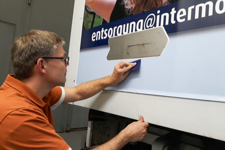 Ein Mitarbeiter arbeitet an der Folierung eines LKWs mit einem Rakel in der Hand.