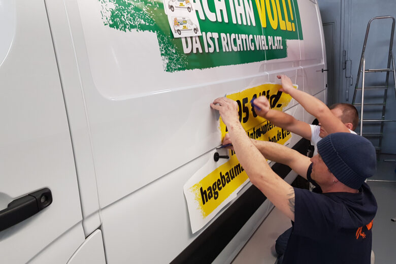 Zwei Personen, die eine Folierung an einem Transportfahrzeug anbringen.