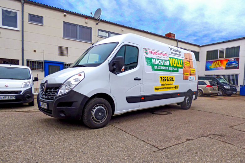 Weißer Renault Transporter mit Werbebeschriftung auf der Seite, geparkt auf einem Parkplatz.