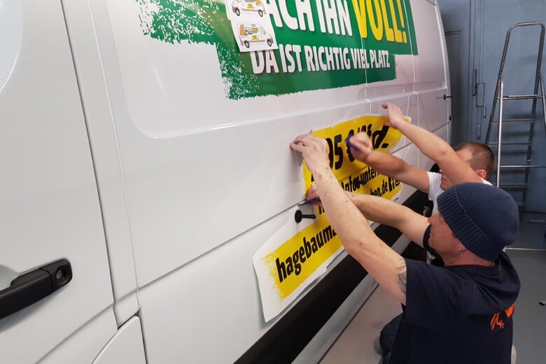 Zwei Mitarbeiter bringen gelbes Werbematerial auf einen weißen Lieferwagen an.