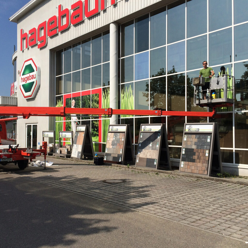 Außenansicht des Hagebau-Marktes mit Musterplatten zur Auswahl, Mitarbeiter auf einer Hebebühne.