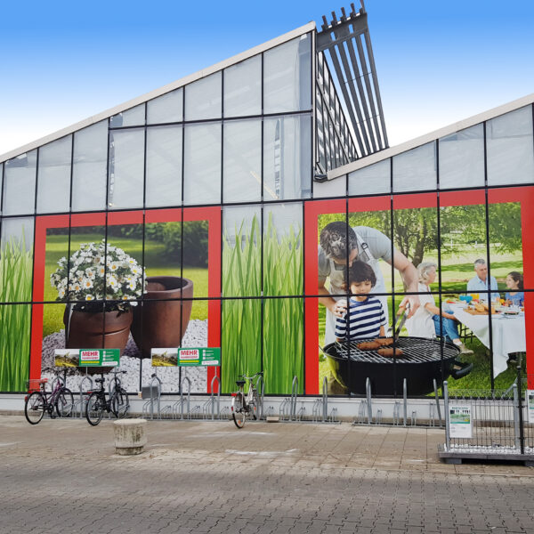 Außenansicht eines Hagebaumarkts mit großen Werbebildern von Pflanzen und Grillaktivitäten.