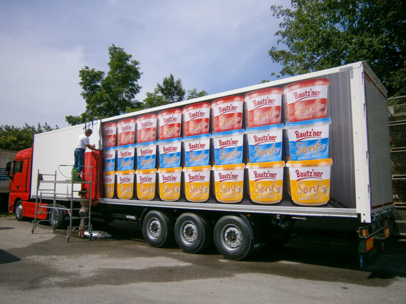 Lkw mit bunten Werbeaufdrucken von Bautzner Senf auf der Ladefläche.