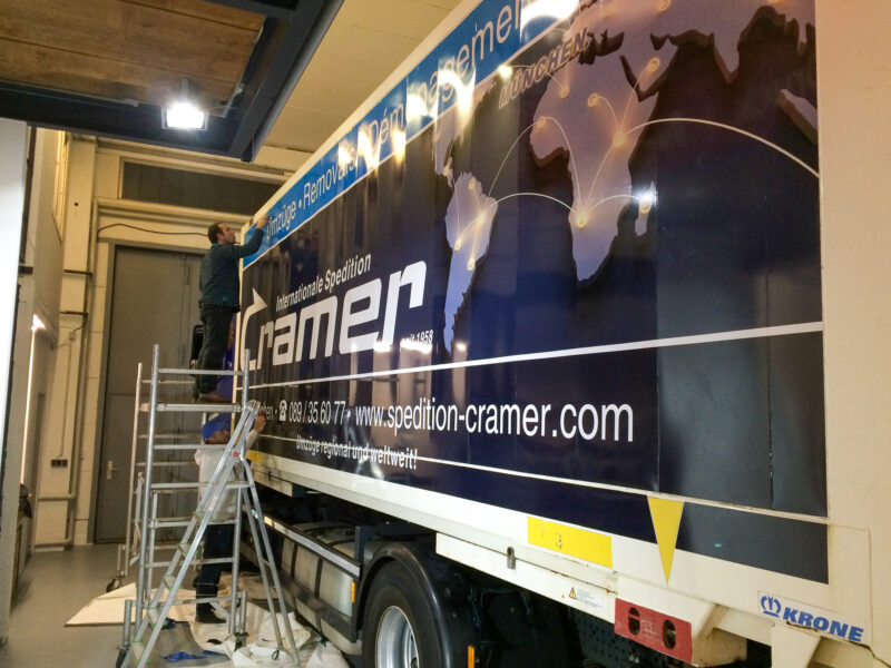 LKW mit der Folierung der Spedition Cramer, während ein Arbeiter an der Wand arbeitet.