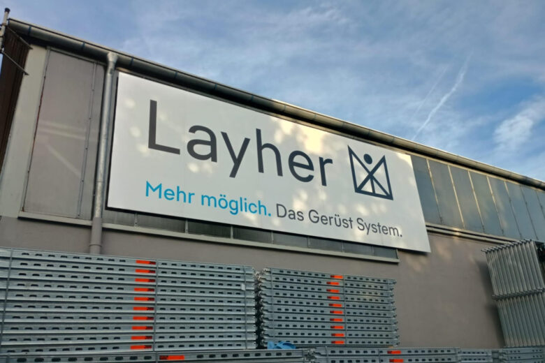 Layher Werbeschild mit dem Slogan 'Mehr möglich. Das Gerüst System.' an einer Wand.