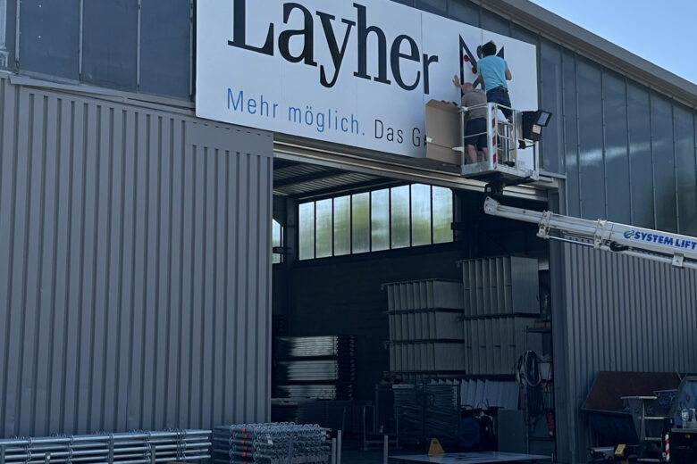 Arbeiter bringt das Layher Firmenlogo an der Fassade eines Gebäudes an.