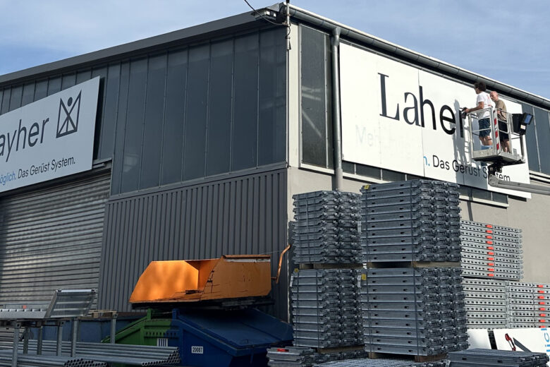 Mitarbeiter montiert ein Werbeschild an der Fassade des Layher Firmengebäudes.
