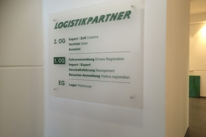 Transparente Beschilderung mit Informationen zu Logistikpartnern in einem Gebäude.