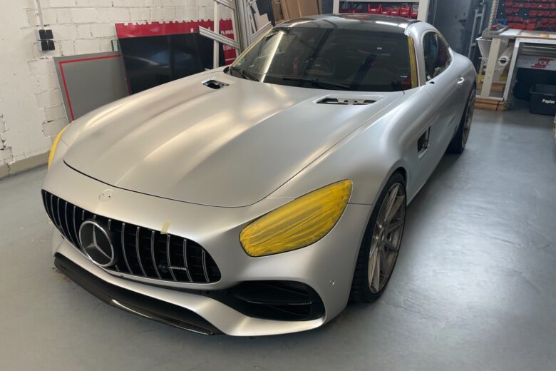 Silberner Mercedes-AMG GT mit gelben Akzenten und Comic-Folierung in einer Werkstatt.