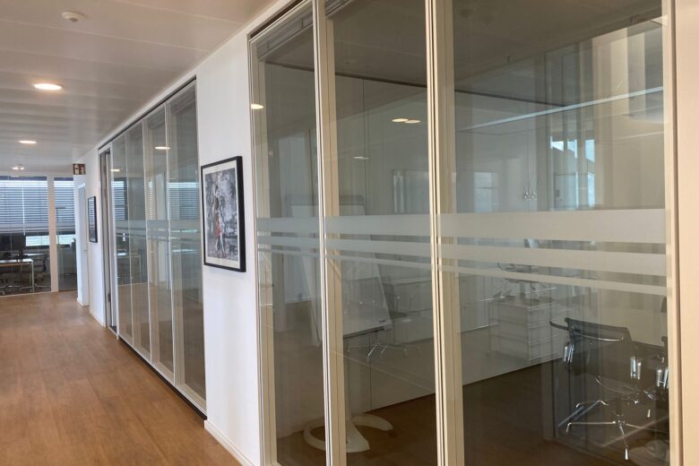 Büro mit Glaswänden und Holzfußboden, das mehrere Besprechungsräume zeigt.