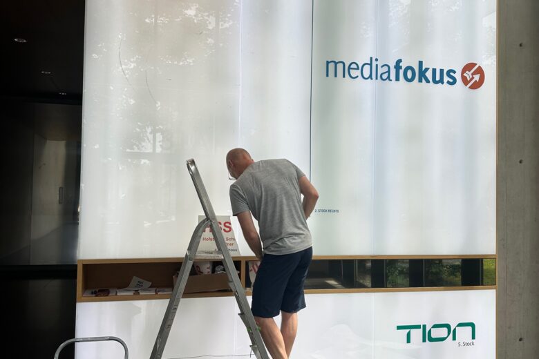 Ein Handwerker arbeitet an einer Wandinstallation mit dem Logo von mediafokus und TION.