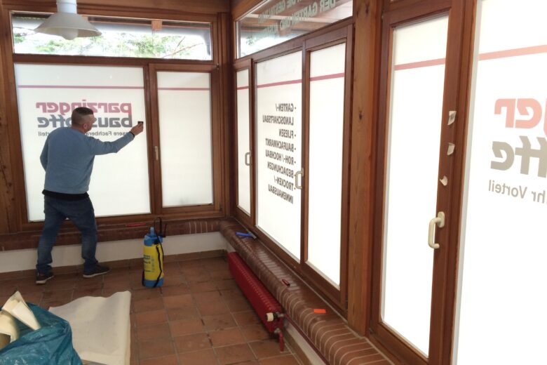 Mitarbeiter installiert Fensterbeschriftungen in einem Innenraum mit Holzverkleidung.