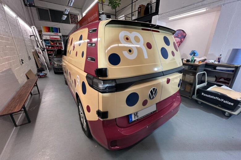 Volkswagen Transporter mit gelbem und rotem Design, verziert mit bunten Punkten und Zahlen.