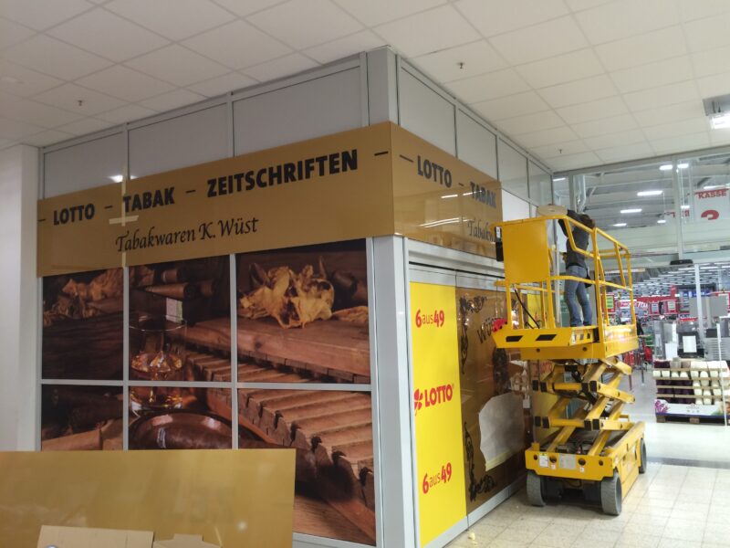 Ein Mitarbeiter montiert ein Schild für das Tabakwaren-Geschäft K. Wüst in einem Verkaufsraum.