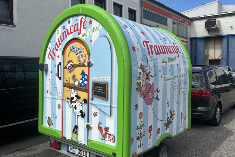 Bunter Verkaufsanhänger des Traumcafes auf Achse mit verschiedenen Illustrationen und einem Fenster für Bestellungen.