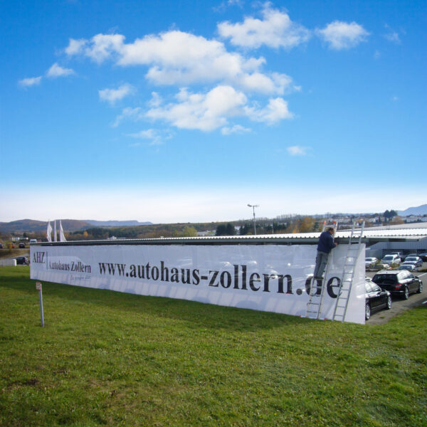 Ein Mitarbeiter montiert ein großes Banner des Autohauses Zollern auf einer Leiter.