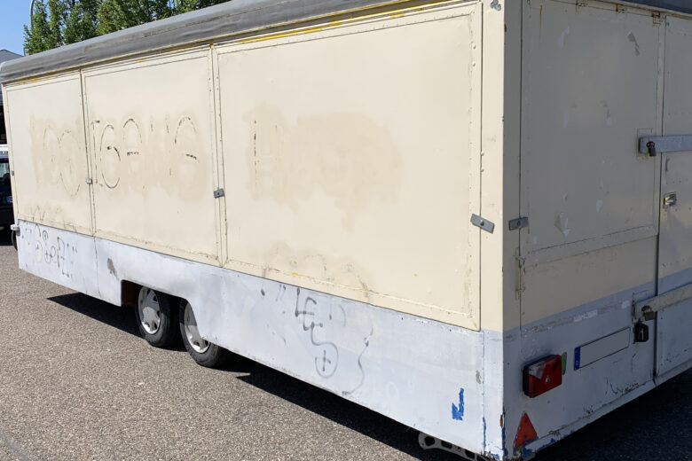 Alter Verkaufsanhänger mit grauem Dach und beige lackierter Oberfläche, sichtbar abgenutzt.