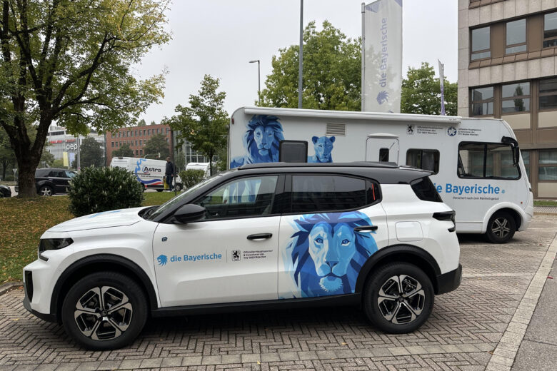 Weißer Citroen mit einem blauen Löwenmotiv, geparkt neben einem Wohnmobil der die Bayerische.