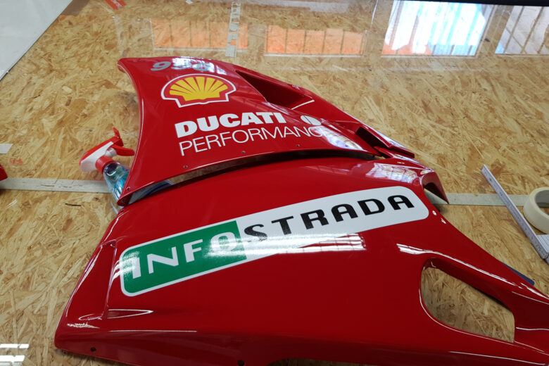Rote Ducati Motorradverkleidung mit Shell und Infostrada Logos auf einer Holzoberfläche.