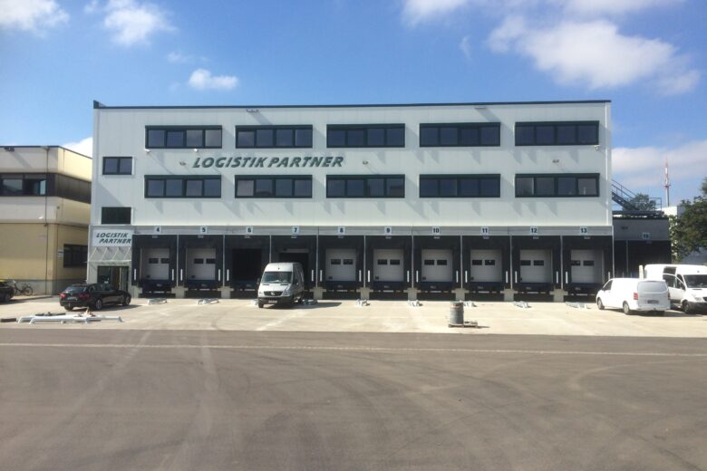 Logistikzentrum mit mehreren Ladebuchten und Fahrzeugen vor dem Gebäude.