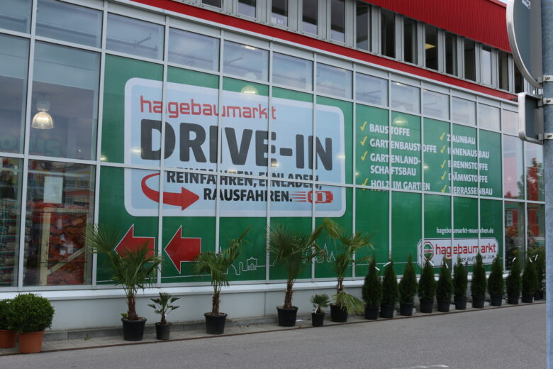 Großes Werbebanner des Hagebaumarkts mit der Aufschrift 'DRIVE-IN' und Pfeilen auf der Fensterfront.