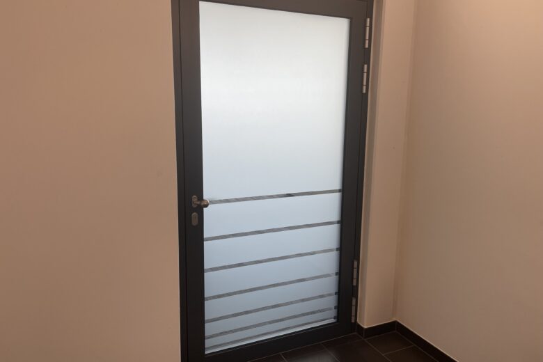 Moderne Glas- und Metalltür mit horizontalen Streben in einem Innenraum.