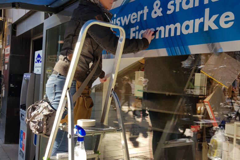 Eine Frau steht auf einer Leiter und bringt ein Schild an einem Geschäft an.