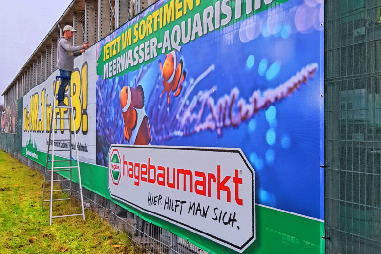 Werbebanner von hagebaumarkt mit Informationen zur Meerwasser-Aquaristik und einem Arbeiter, der daran arbeitet.