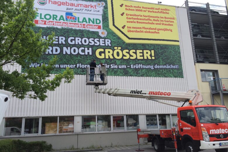Großes Werbebanner von hagebaumarkt, das Floraland bewirbt, mit einem Mitarbeiter in einem Hubsteiger.