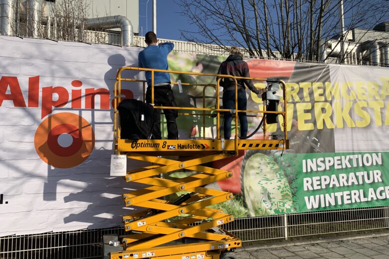 Arbeiter auf einer Hebebühne, die ein großes Werbebanner anbringen.