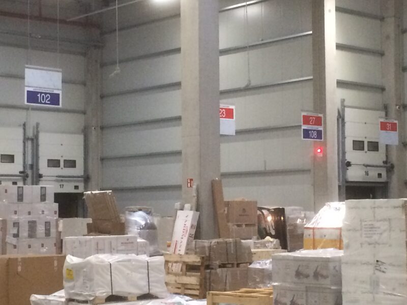 Lagerbereich mit Paletten und Regalen, nummeriert mit Schildern 23, 27, 102, 108 und 311.