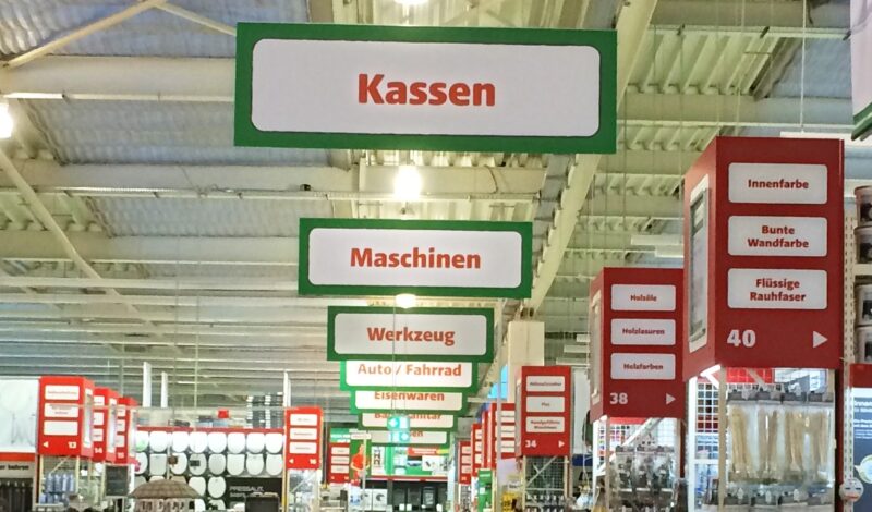 Hängende Schilder mit den Aufschriften Kassen, Maschinen, Werkzeug im Einzelhandel.