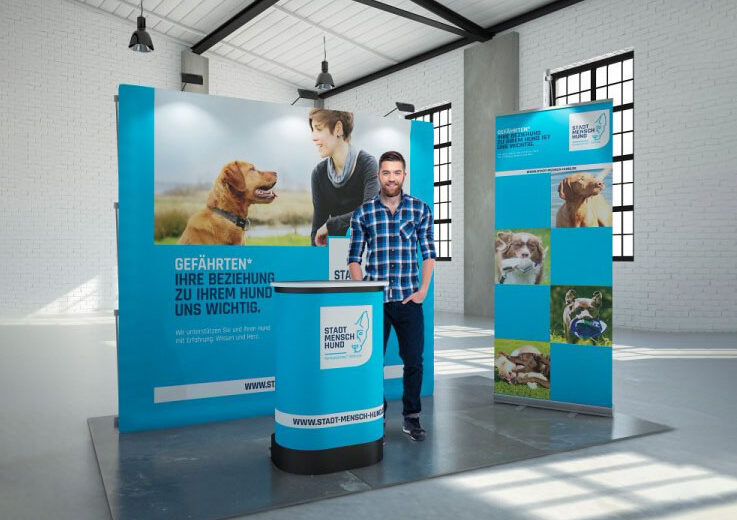 Messestand mit einem Mann und einem Hund, der Informationen zu Hundebeziehungen bereitstellt.
