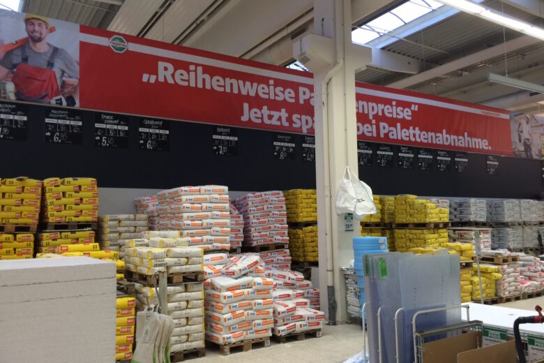 Lagerbereich mit verschiedenen Baustellenmaterialien und einem großen Werbebanner an der Wand.