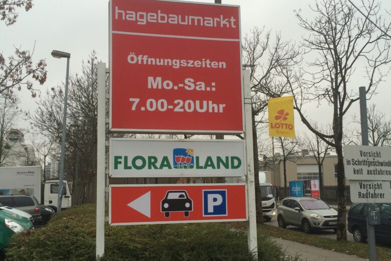 Schild mit Öffnungszeiten für Hagebaumarkt und Flora Land, inklusive Parkplatzinformation.
