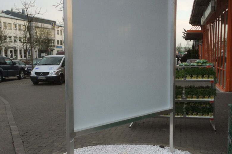 Leerer Werbepylon mit einem Aluminiumrahmen auf einem Gehweg, umgeben von weißen Kieselsteinen.