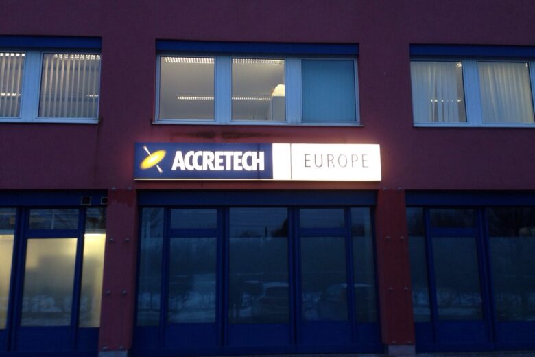 Firmenschild von Accretech Europa an einem Gebäude mit blauen Fenstern.