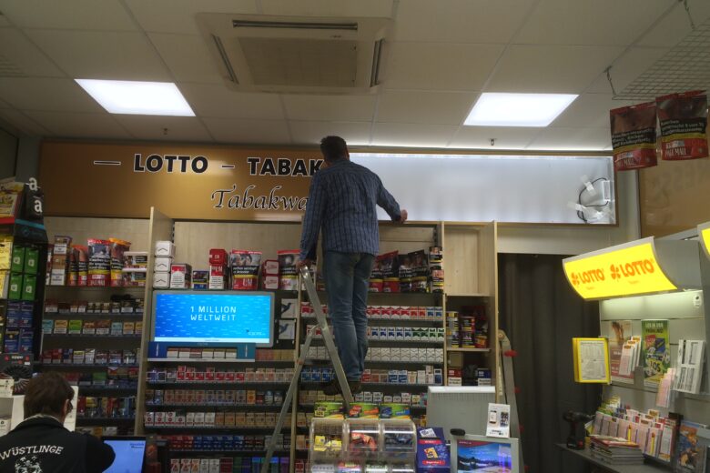 Mitarbeiter auf einer Leiter im Tabakgeschäft, während er an einem Regal arbeitet.