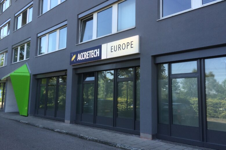 Fassade des Accretech Europa Bürogebäudes mit großen Fenstern und einem grünen Element.