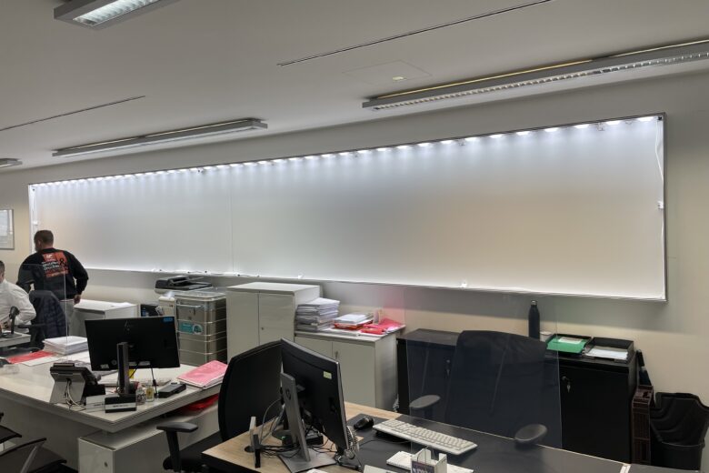 Leuchtkasten mit Textilspannrahmen, beleuchtet und an einer Wand montiert, in einem Büro.