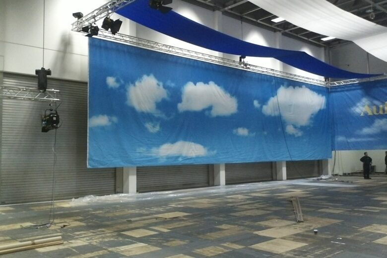 Großes Werbebanner mit einem blauen Himmel und weißen Wolken, aufgehängt in einem Innenraum.