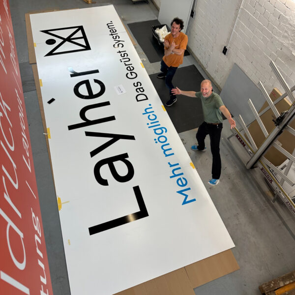 Großes Werbeschild mit dem Schriftzug 'Layher' und dem Slogan 'Mehr möglich. Das Gerüst System.'