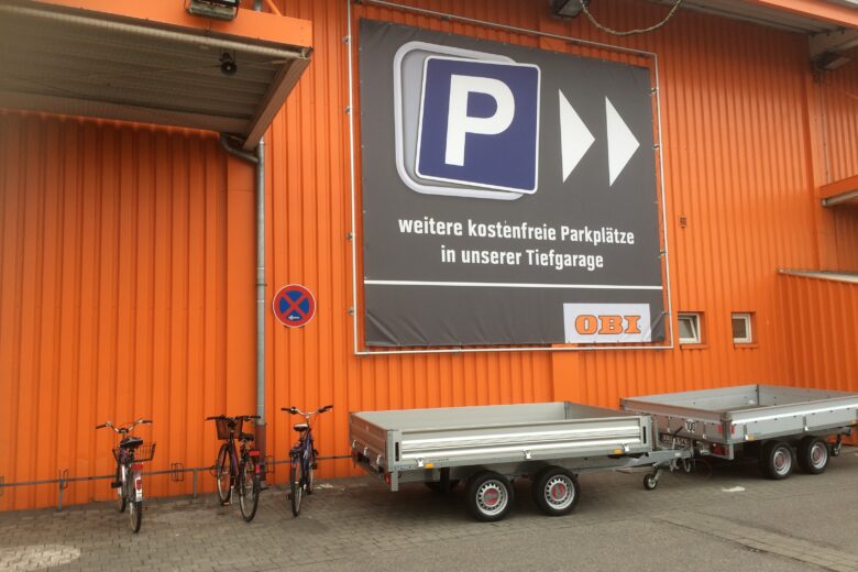 Banner mit Parkplatzinformationen an der Außenwand einer OBI-Filiale, orangefarbener Hintergrund.